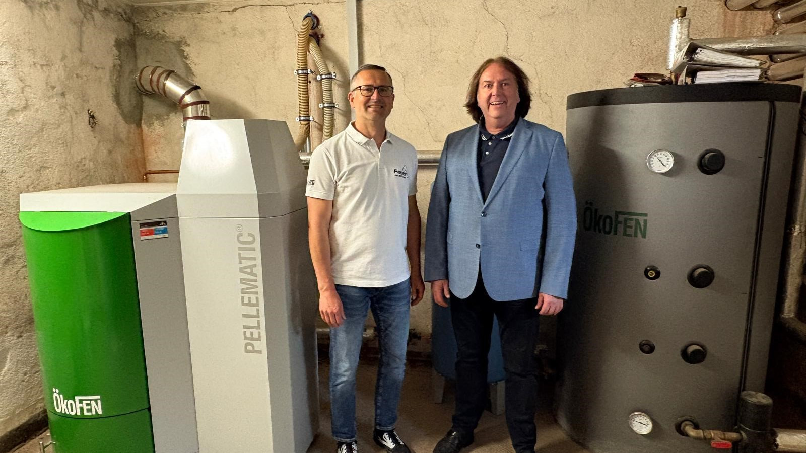 Zwei Männer neben einem ÖkoFEN Pellematic-Heizsystem in einem Keller.